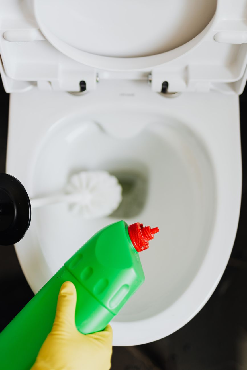 crop person cleaning toilet with detergent and brush