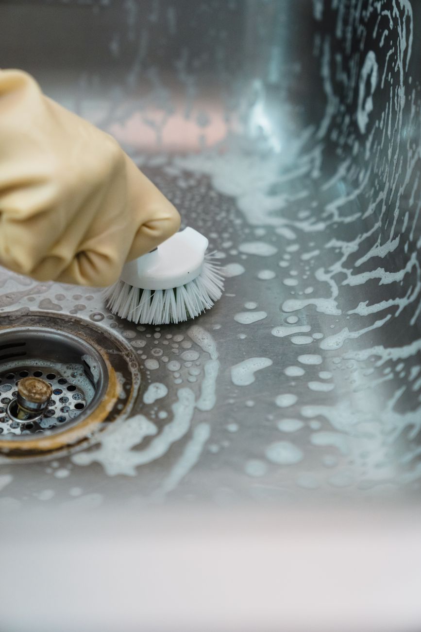 a person in yellow rubber gloves cleaning stainless sink
