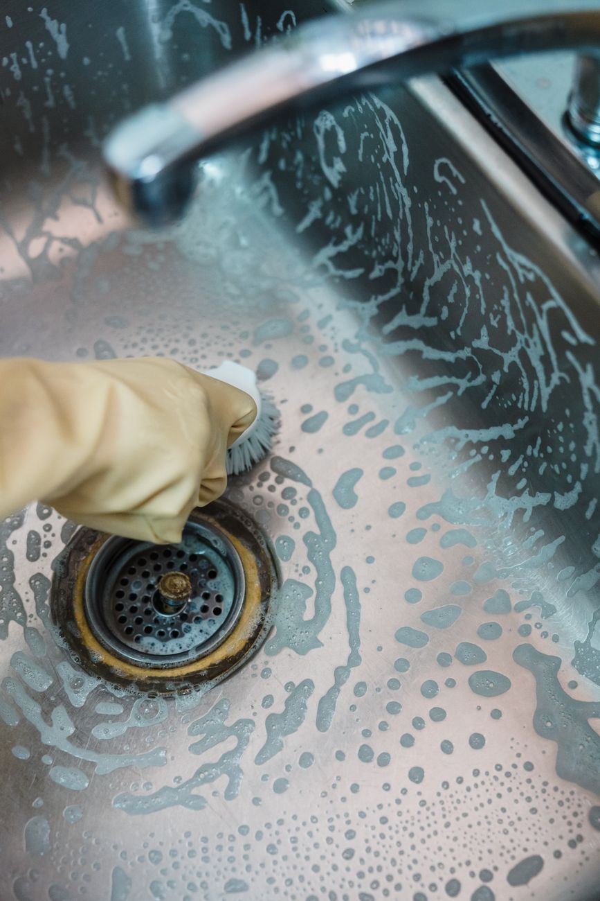 person in yellow gloves cleaning stainless sink